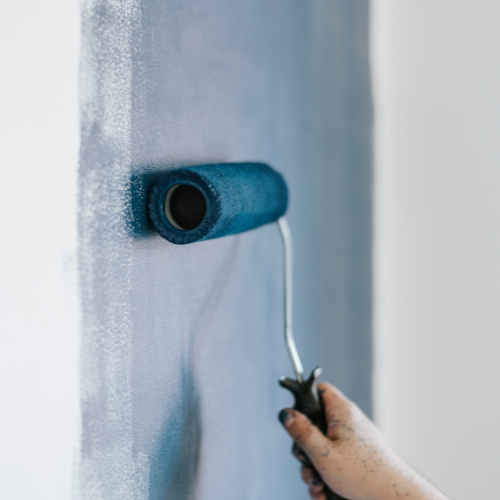 A close up of a blue paint roller painting a wall